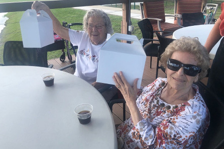2 older women holding up box lunches