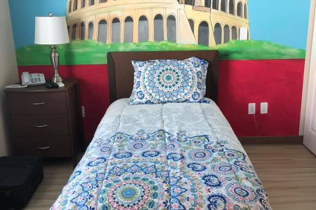 A bed and end table in front of a mural of the Colosseum in ancient Rome