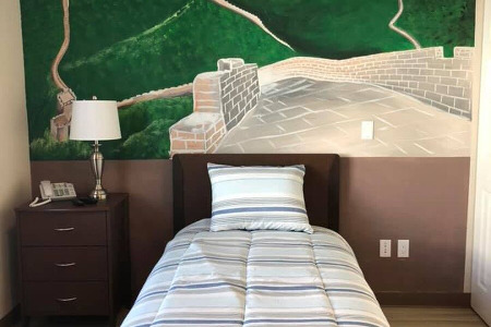 Bed and end table in front of mural of the Great Wall of China