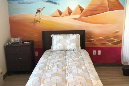 Bed and end table in front of mural of Egyptian Pyramids   